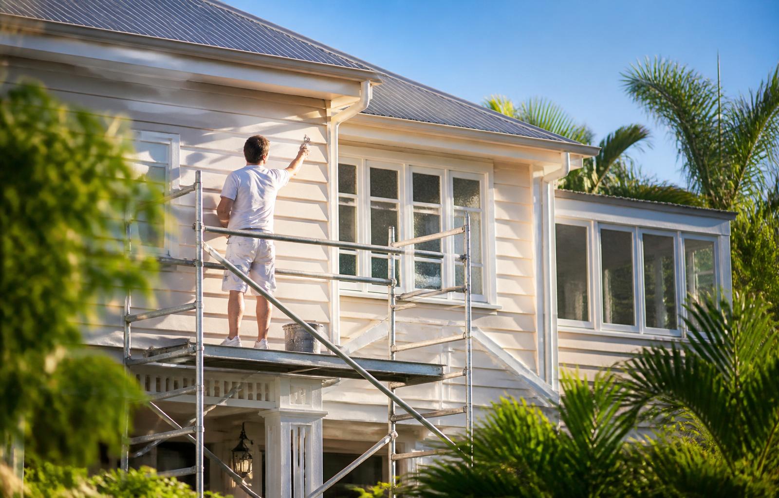 Professional painter on scaffolding applying fresh paint to a Queenslander-style home in North Brisbane